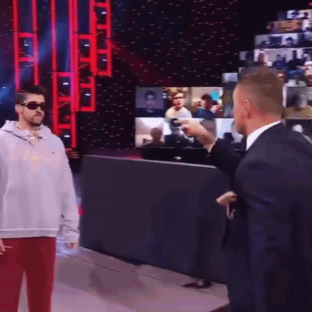 a man in a suit is standing next to a man in a sweatshirt on a stage .