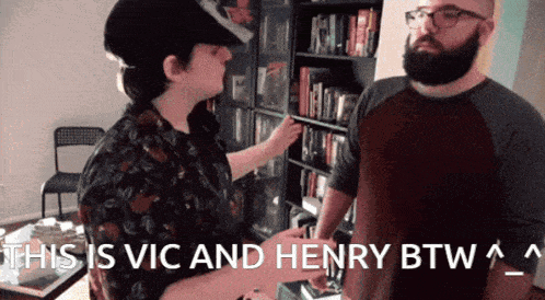 a man and a woman are standing in front of a bookshelf with the words this is vic and henry btw
