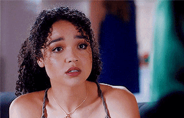 a woman with curly hair is wearing a necklace and sitting on a couch .