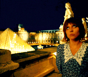 a woman is standing in front of a pyramid at night