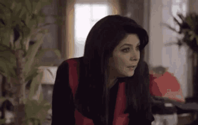 a woman is sitting in a living room with a plant in the background and looking at the camera .
