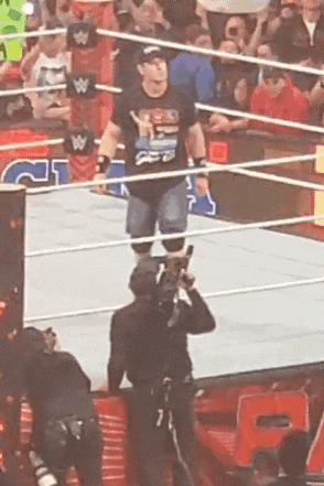 a man is standing in a wrestling ring while a cameraman takes a picture .