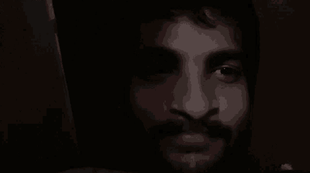 a close up of a man 's face with a beard in the dark