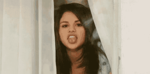 a woman is sticking her tongue out while peeking through a curtain .