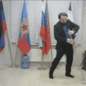 a man in a suit is dancing in a room with flags in the background