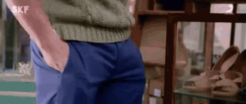 a man in a green sweater and blue pants is standing with his hands in his pockets in a store .