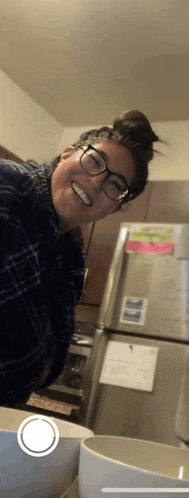 a woman with glasses is smiling in front of a refrigerator