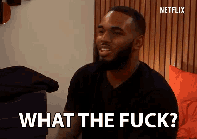 a man with a beard is sitting on a bed and says what the fuck
