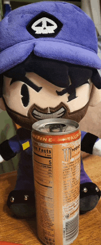 a can of monster energy drink sits next to a stuffed animal
