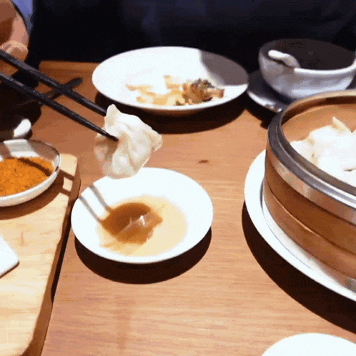 a person dipping a dumpling with chopsticks in a dipping sauce
