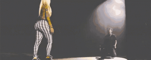 a woman in plaid pants is dancing on a stage while a man stands behind her