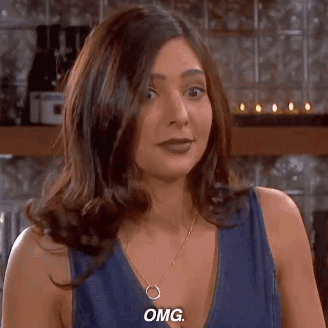 a woman wearing a blue tank top and a gold necklace is saying omg