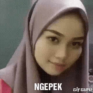 a woman wearing a hijab and a pink shirt is smiling and making a funny face .