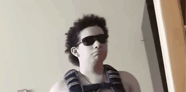 a young man wearing sunglasses and a backpack is standing in front of a wall .