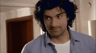 a man with curly hair and a blue shirt is looking at the camera .