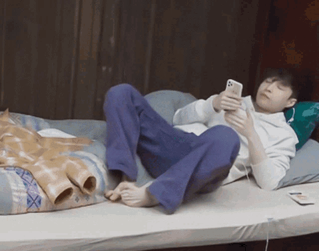 a man is laying on a bed looking at his cell phone