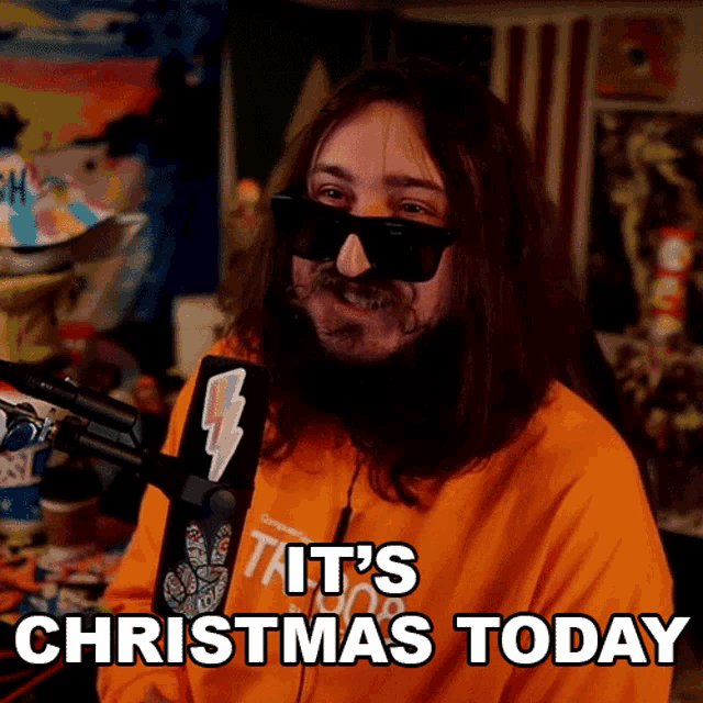 a man with long hair and a beard says it 's christmas today in front of a microphone