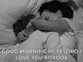 a black and white photo of a man and woman hugging each other in bed .