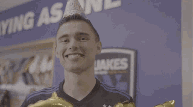 a man wearing a birthday hat holds up balloons that spell out the word birthday