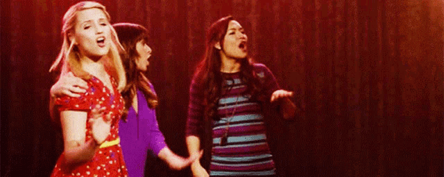 three women are singing together on a stage
