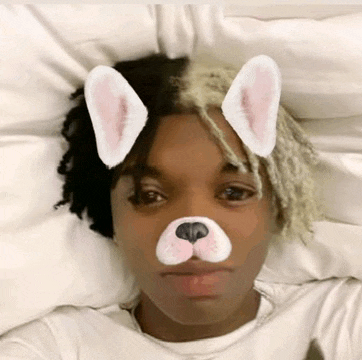 a young man with bunny ears on his face is laying on a bed .