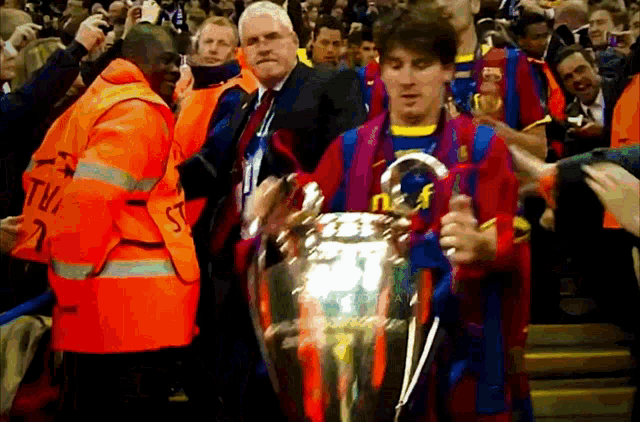 a man in an orange vest with the letter t on it holds a trophy
