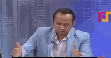 a man in a blue suit is sitting at a desk with a microphone in front of a tv screen that says news