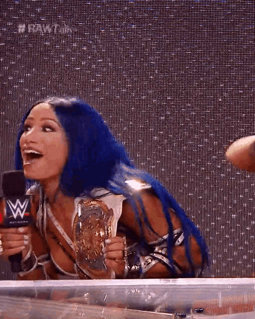a woman with blue hair is holding a wrestling championship and laughing .