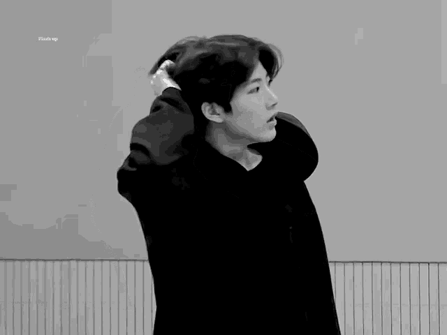a black and white photo of a young man in a hoodie holding his hair .