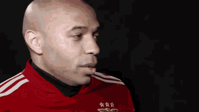 a bald man wearing a red shirt with three stars on it is looking at the camera .