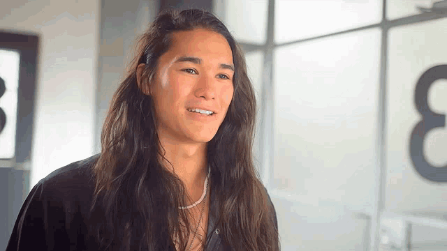 a young man with long hair is smiling in front of a sign that says ' 3 '