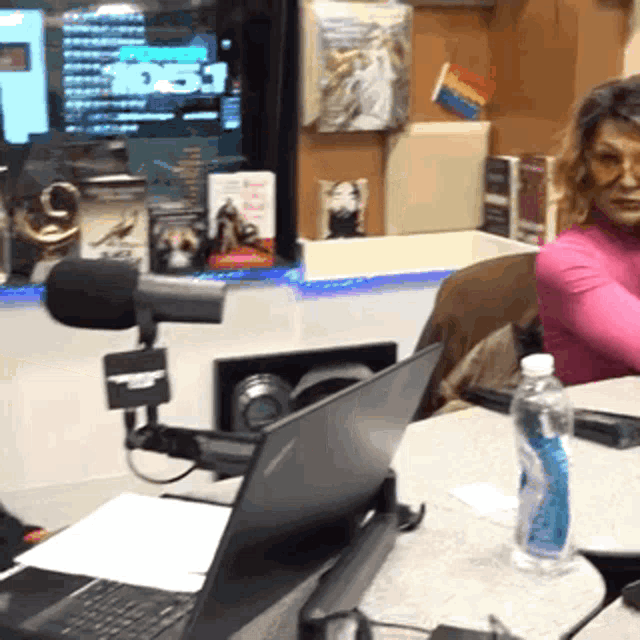 a woman sits at a desk with a laptop and a bottle of water in front of a screen that says 1051