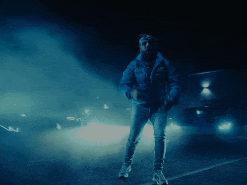 a man in a blue jacket is standing in a parking lot with cars in the background