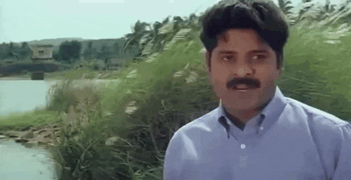 a man with a mustache is standing next to a body of water .