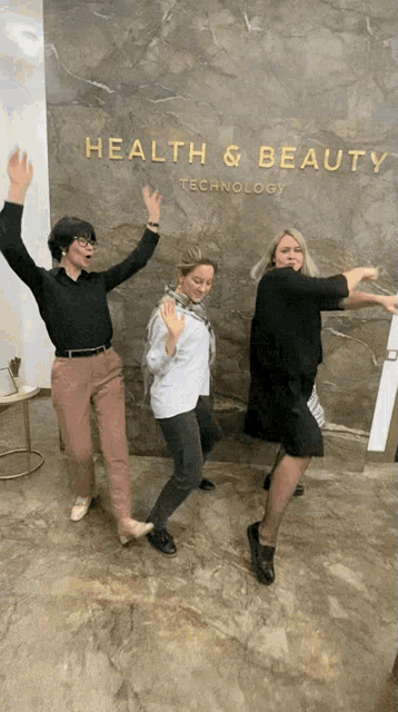 three women are standing in front of a wall that says health & beauty technology