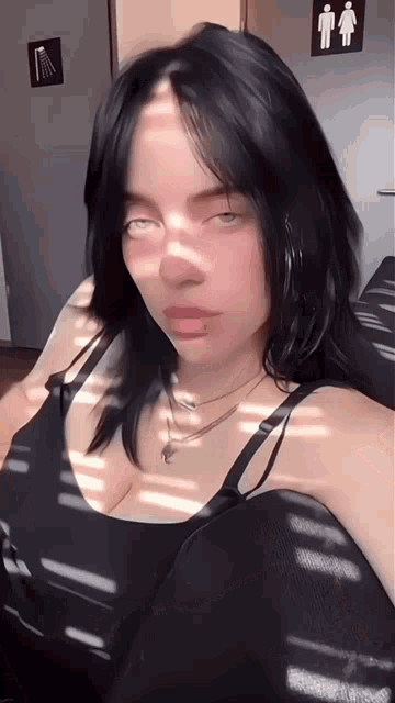 billie eilish is wearing a black tank top and a necklace while taking a selfie .