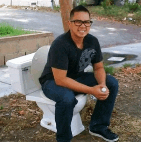 a man wearing glasses is sitting on a toilet in the dirt .