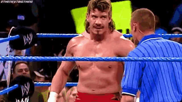 a wrestler is standing in the middle of a wrestling ring talking to a referee .