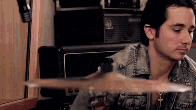 a man in a denim jacket plays a drum set