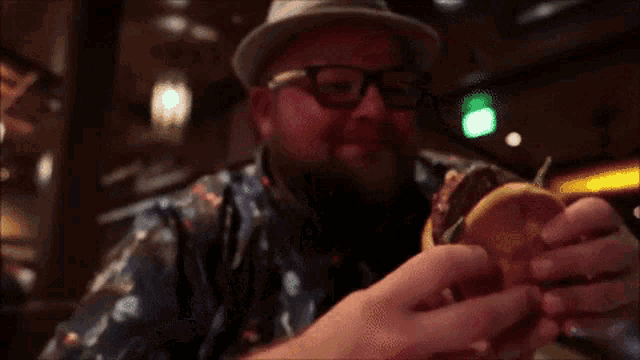 a man wearing a hat and glasses eating a hamburger