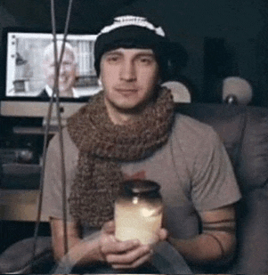 a man wearing a scarf and a hat is holding a jar of honey .