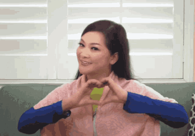 a woman making a heart with her hands in front of a window