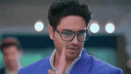 a man wearing glasses and a blue suit is standing in a room .