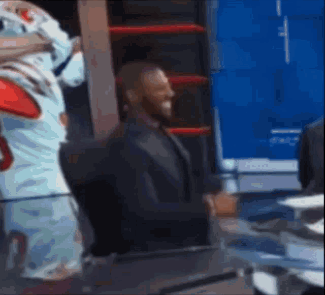 a man in a suit is standing next to a mascot in a boxing ring .