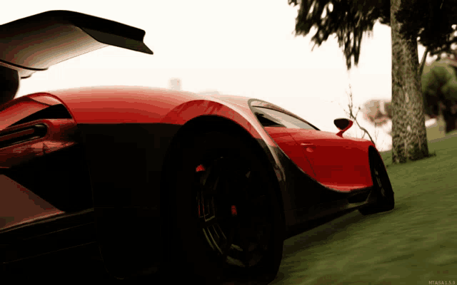 a red sports car is parked in a grassy area with a tree in the background