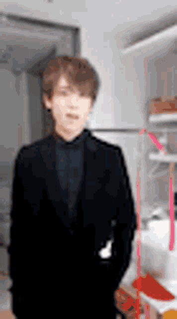 a man in a suit and tie is standing in a room with his hands in his pockets .