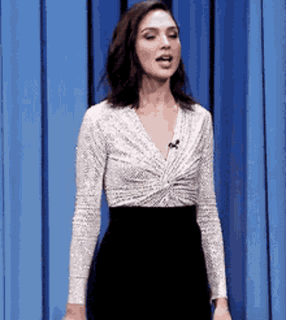 a woman is standing in front of a blue curtain wearing a white top and black skirt .