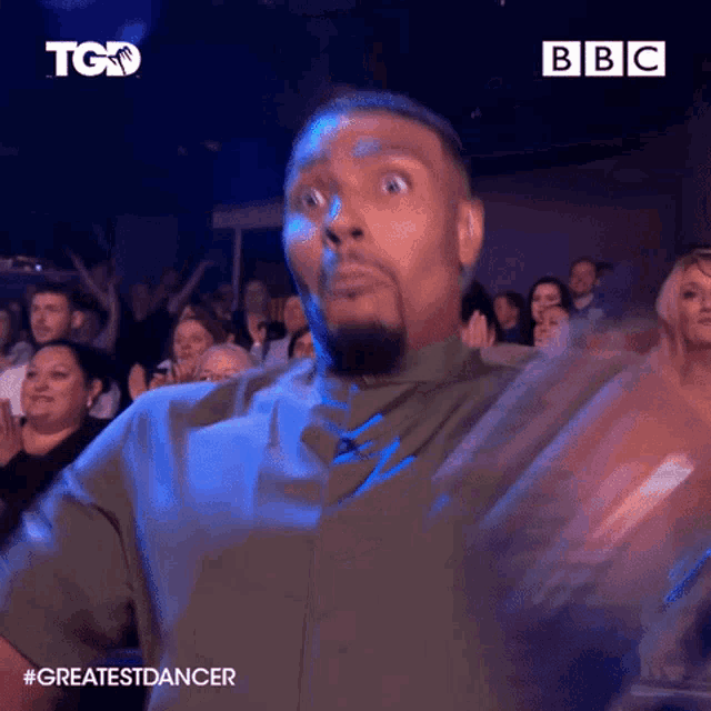 a man with a beard is dancing in front of a crowd with a bbc logo in the background