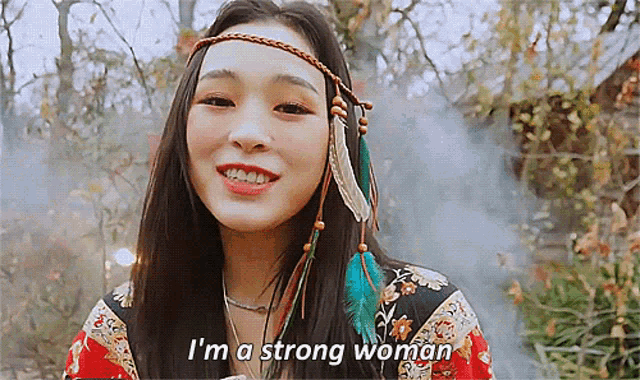 a woman with feathers in her hair is smiling and says " i 'm a strong woman "
