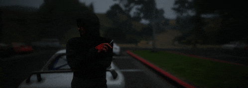 a man in a black hoodie is standing in front of a car